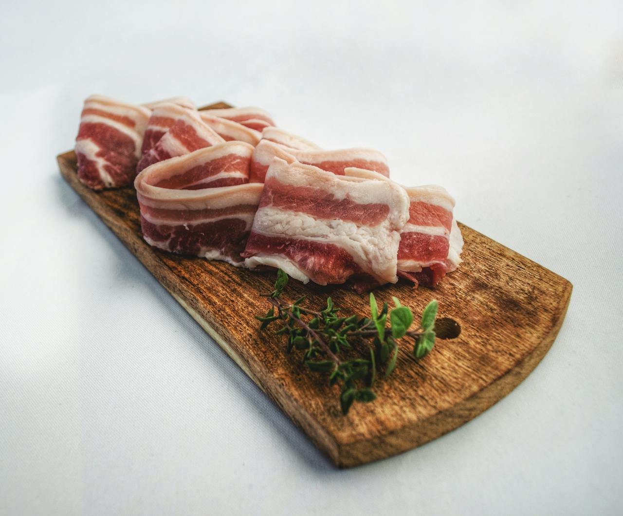 Carnicería en Sort de calidad. Sliced bacon laid on a rustic wooden board with herbs, showcasing a delicious and inviting food presentation.