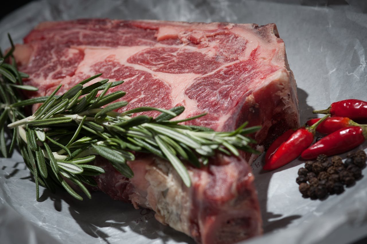 Productos cárnicos en Sort. Close-up of a raw steak garnished with rosemary and chilies, ideal for cooking concepts.