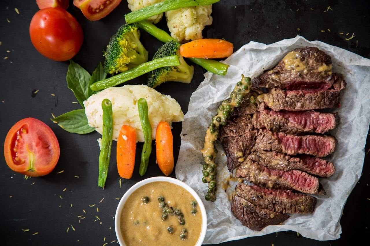 Productos cárnicos en Sort. Grilled steak served with fresh vegetables and pepper sauce, presenting a colorful and appetizing meal.